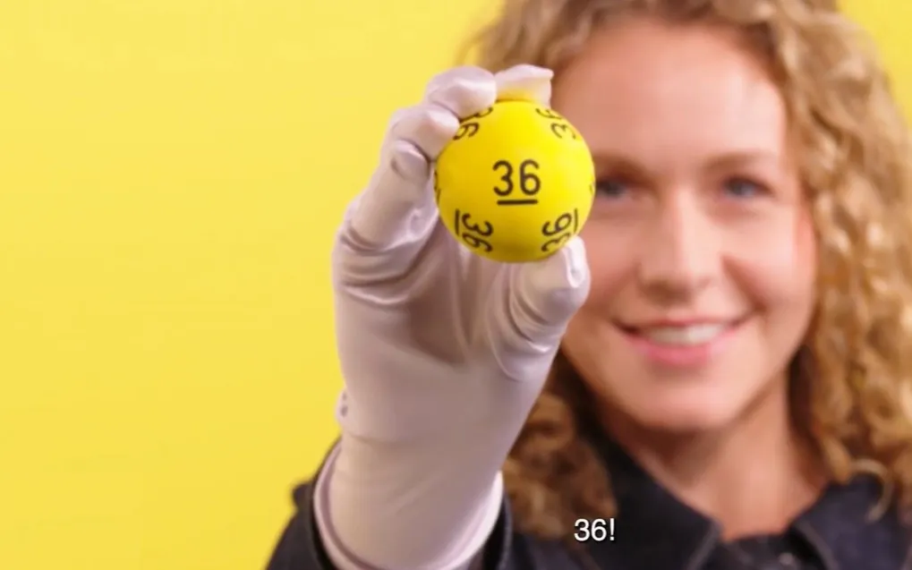 Persoon houdt een gele bal vast met het nummer 36, op een gele achtergrond.