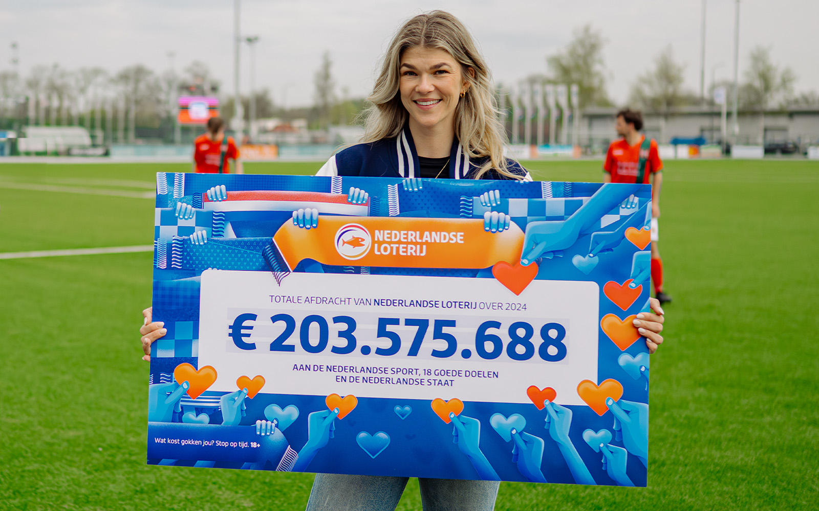 Persoon houdt een bord vast met totale afdracht van Nederlandse Lotto over 2024, 203575688 euro voor sport en goede doelen.