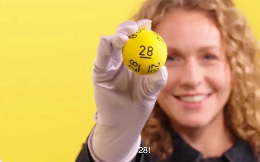 Hand houdt een gele bal met het nummer 28 omhoog voor een gele achtergrond.