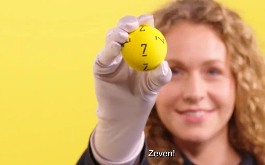Een hand met een gele bal met het nummer 7 op een gele achtergrond.