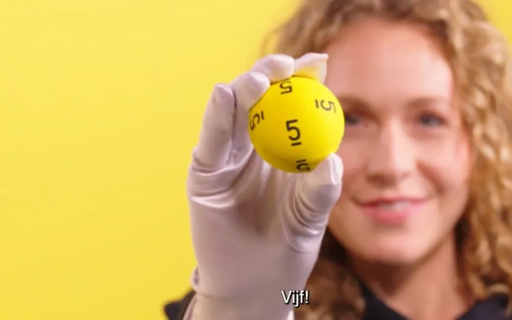 Gele bal met het nummer 5, gehouden door een persoon met handschoenen.