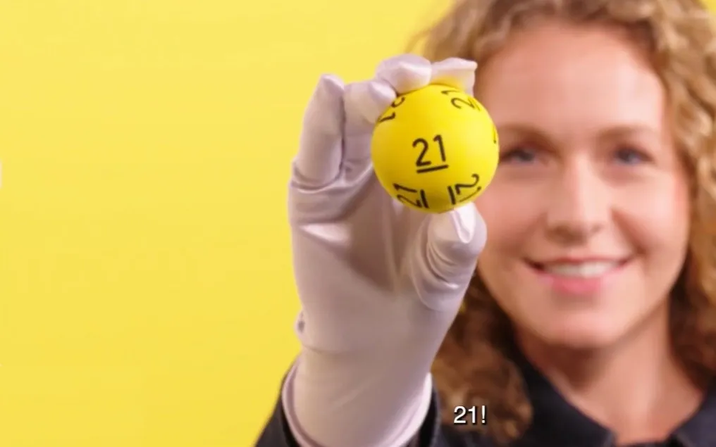 Een hand houdt een gele bal met het nummer 21 omhoog voor een gele achtergrond.