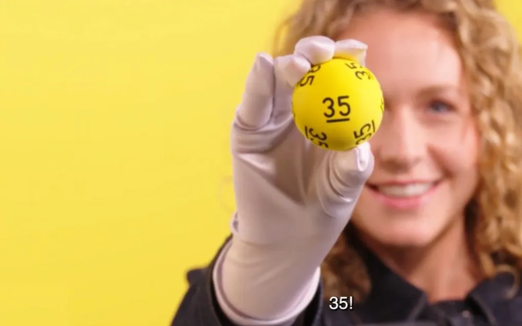 Persoon houdt een gele bal met het nummer 35 omhoog voor een gele achtergrond.