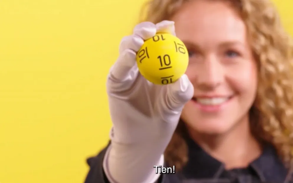 Een persoon toont een gele bal met het nummer 10 op een gele achtergrond.