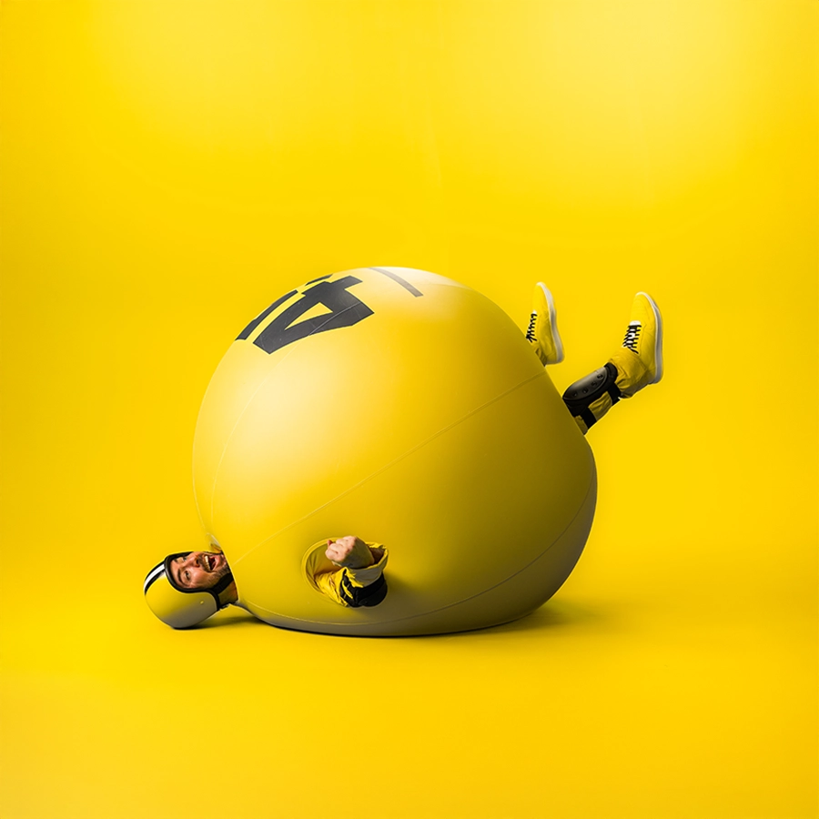 Persoon in een grote gele bal met het nummer 47, op een gele achtergrond.