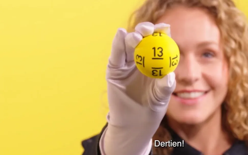 Een persoon die een gele bal met het nummer 13 vasthoudt, tegen een gele achtergrond.