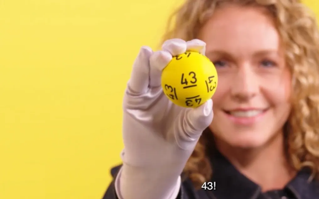 Hand houdt een gele bal met het nummer 43 omhoog tegen een gele achtergrond.