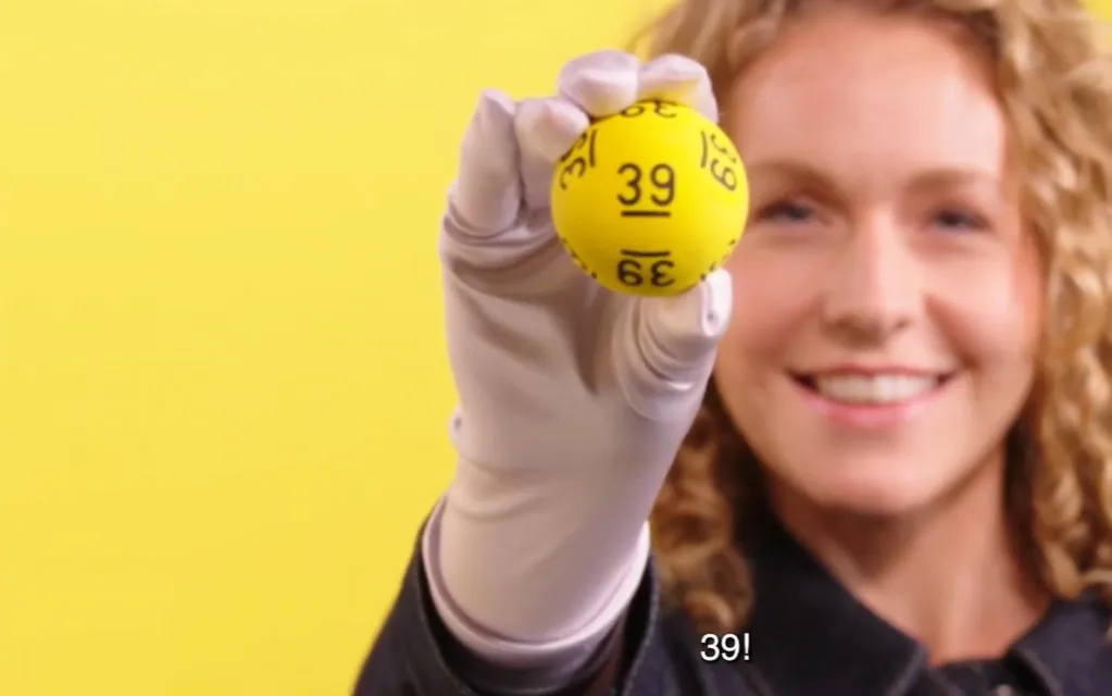 Een hand houdt een gele bal met het nummer 39, op een gele achtergrond.