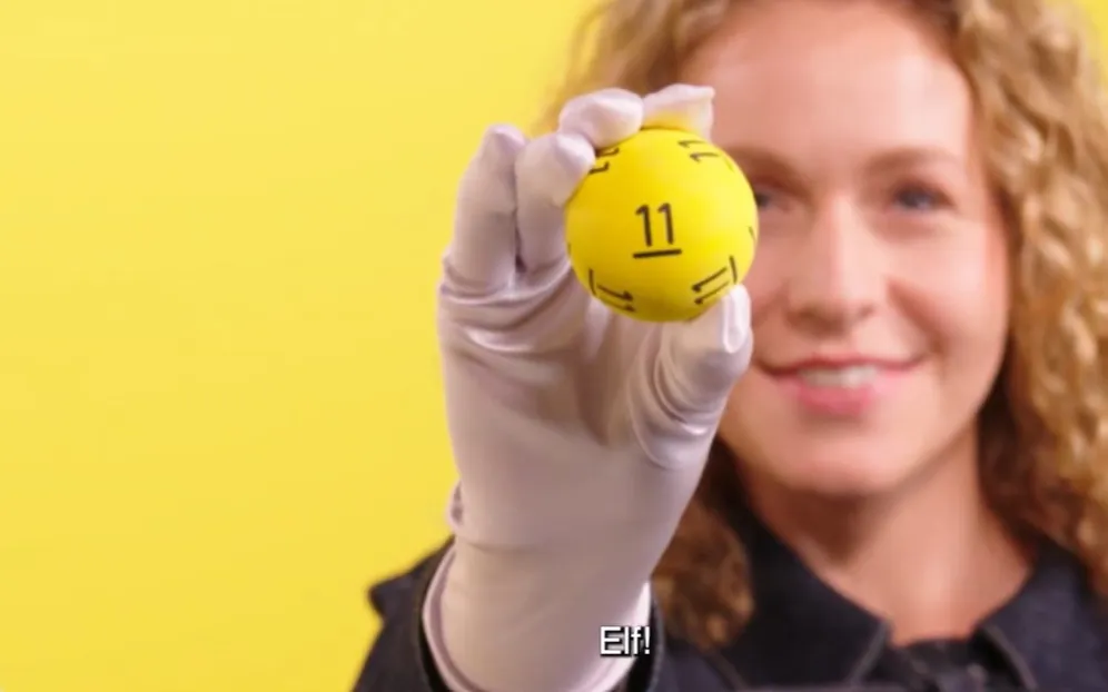 Een hand die een gele bal met het nummer 11 vasthoudt, op een gele achtergrond.