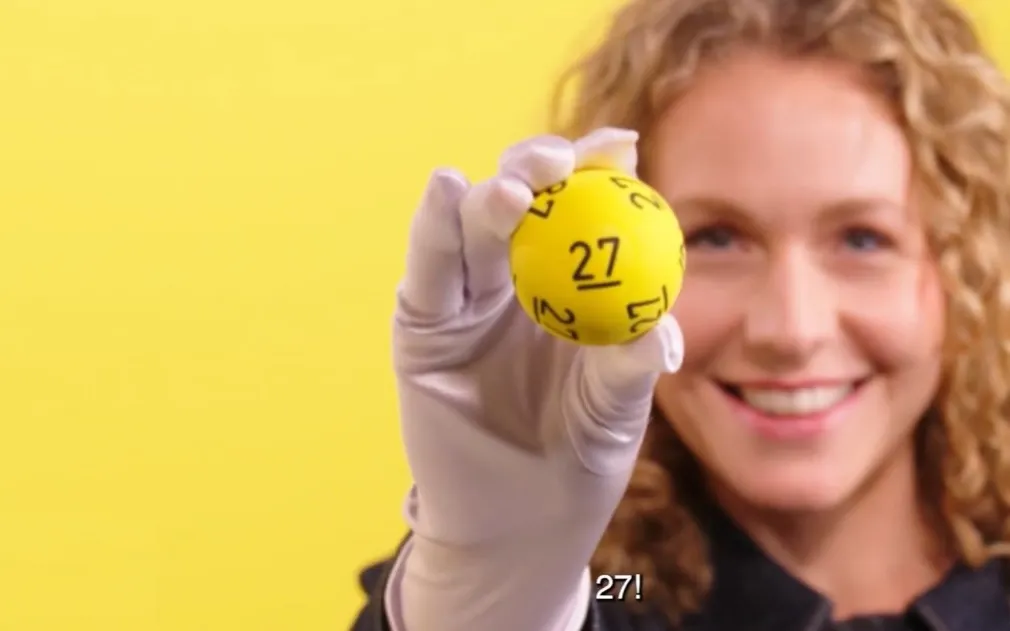 Een persoon houdt een gele bal omhoog met het nummer 27 erop.