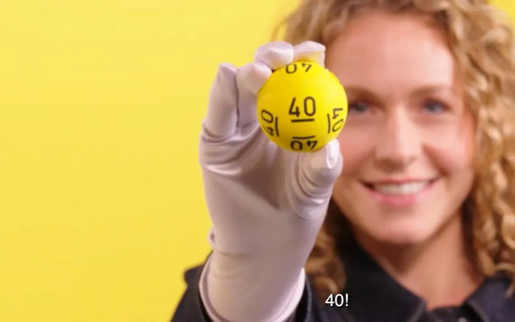Een hand houdt een gele bal met het nummer 40 omhoog tegen een gele achtergrond.