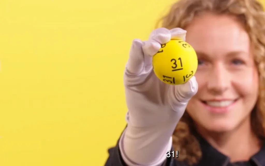 Een gele bal met het nummer 31, vastgehouden door iemand met een witte handschoen, met een gele achtergrond.