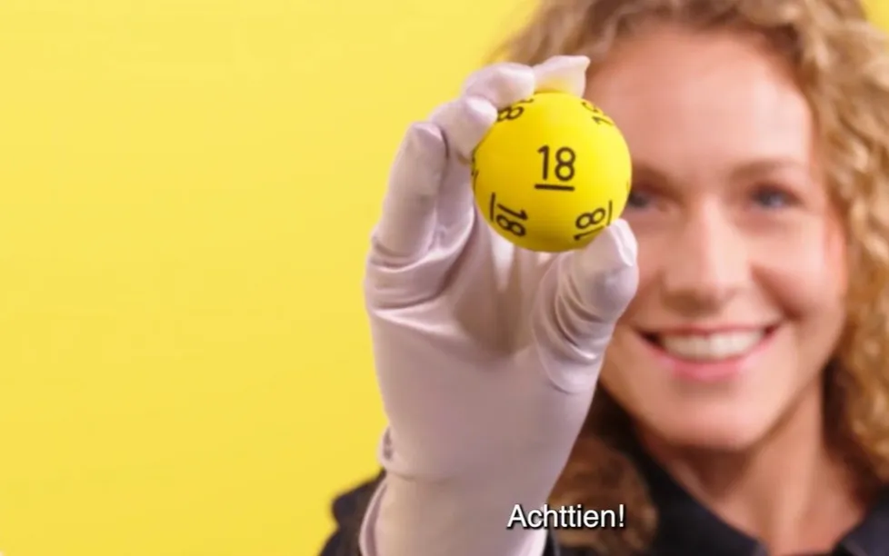 Gele bal met het nummer 18, vastgehouden door een persoon in een witte handschoen.