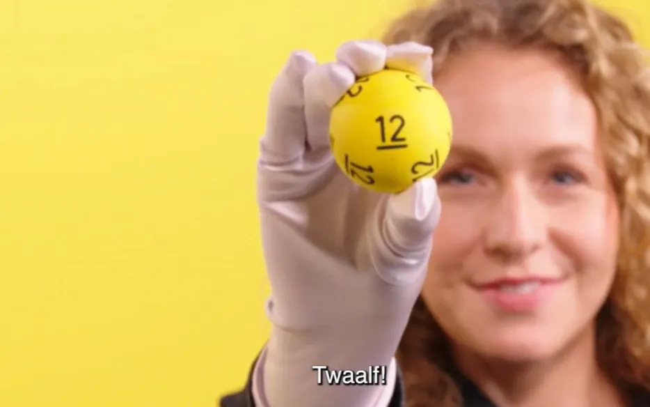 Een hand met een gele bal met het nummer 12, tegen een gele achtergrond.