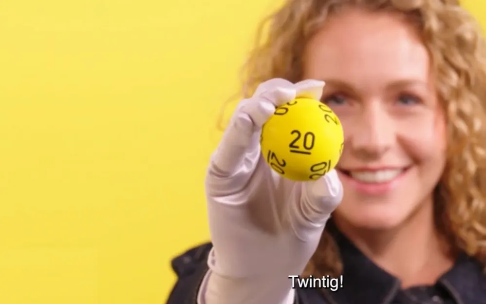 Persoon houdt een gele bal met het nummer 20 omhoog voor een gele achtergrond.